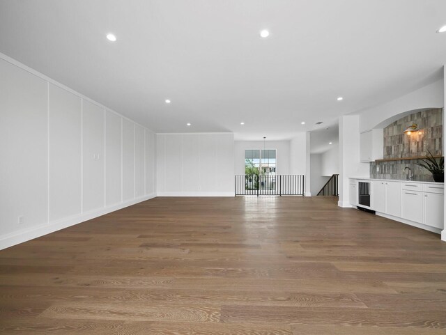 unfurnished living room featuring wood finished floors, bar, recessed lighting, a decorative wall, and a chandelier