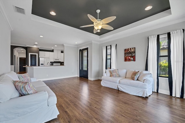 living room featuring ceiling fan, a raised ceiling, crown molding, and dark wood-type flooring