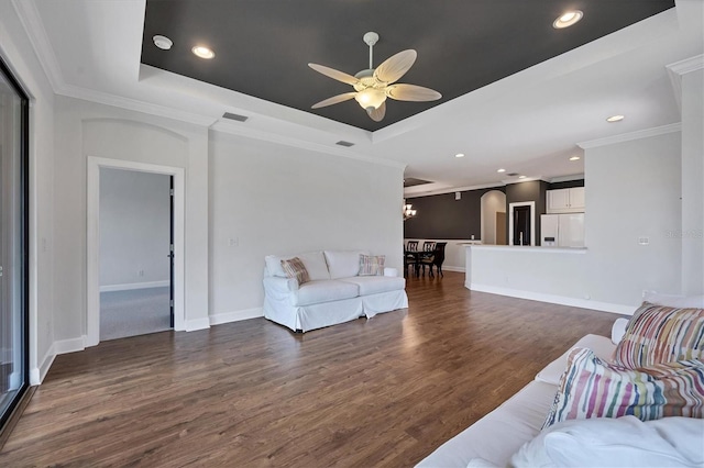 living room with dark wood-type flooring, ceiling fan, ornamental molding, and a tray ceiling