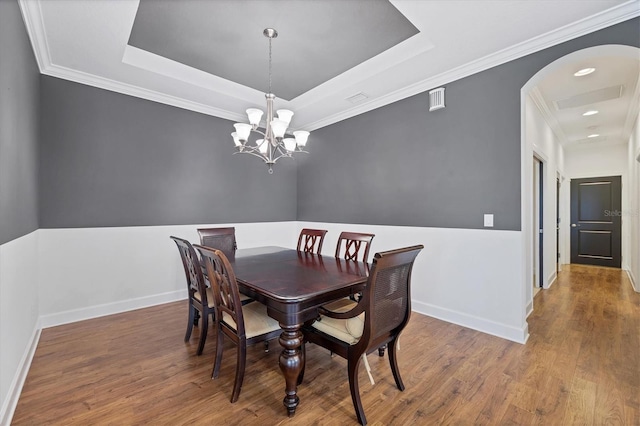 dining area with an inviting chandelier, a raised ceiling, and hardwood / wood-style floors