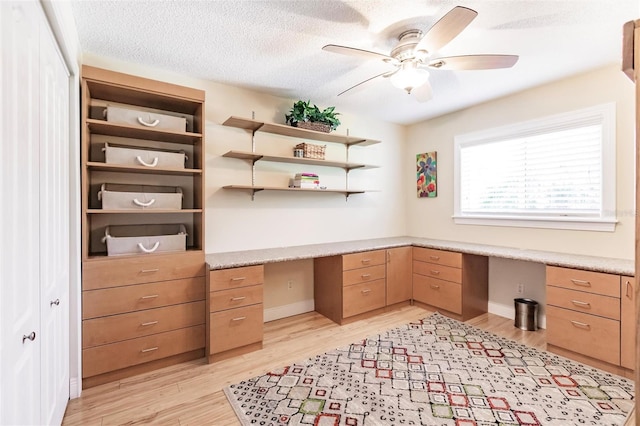 home office featuring built in desk, a textured ceiling, light hardwood / wood-style floors, and ceiling fan