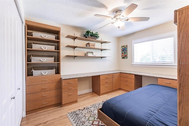 bedroom featuring light wood-type flooring, built in desk, a textured ceiling, and ceiling fan