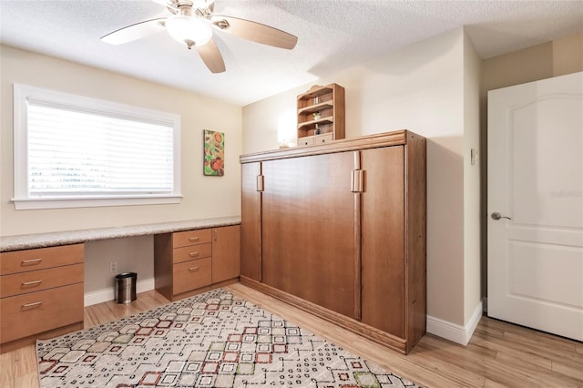 office area featuring light wood-type flooring, built in desk, a textured ceiling, and ceiling fan