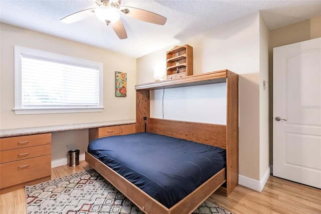 bedroom with built in desk, a textured ceiling, ceiling fan, and light hardwood / wood-style flooring