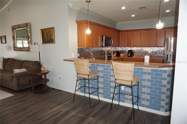 kitchen with dark wood-type flooring, hanging light fixtures, appliances with stainless steel finishes, a kitchen bar, and kitchen peninsula