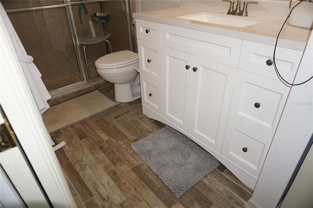 bathroom featuring wood-type flooring, vanity, toilet, and a shower with shower door