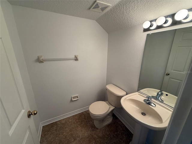 half bath with a textured ceiling, visible vents, a sink, toilet, and lofted ceiling