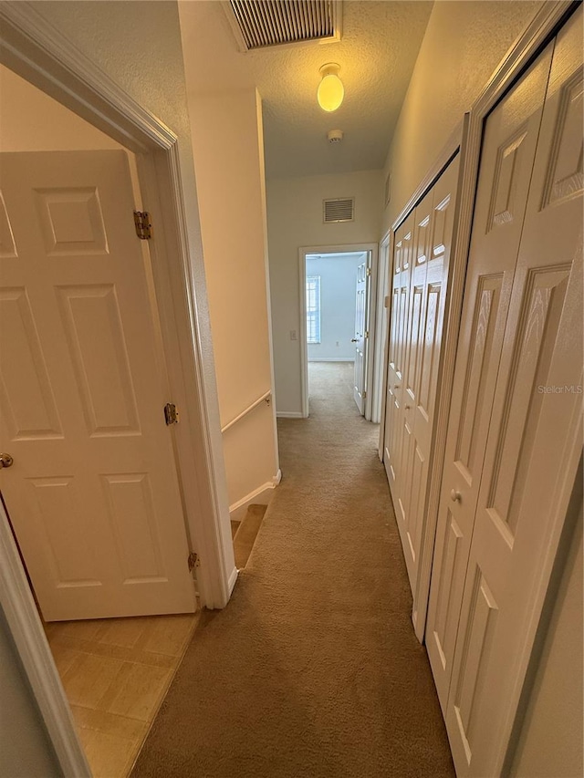 hall with baseboards, light colored carpet, and visible vents