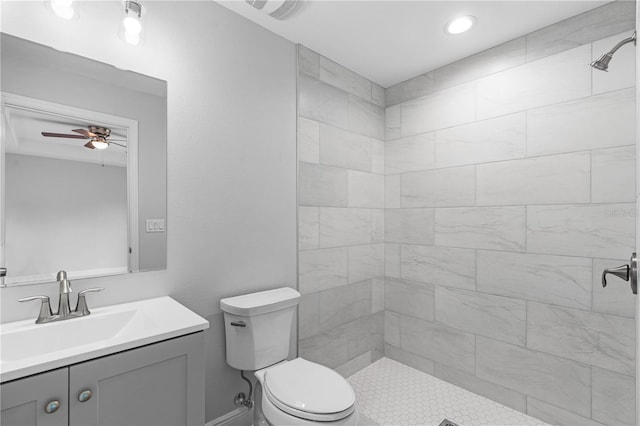 bathroom featuring a tile shower, ceiling fan, vanity with extensive cabinet space, and toilet