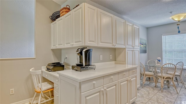 kitchen with white cabinets, a textured ceiling, light tile floors, and built in desk