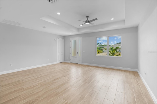 unfurnished room with ceiling fan, light hardwood / wood-style floors, and a tray ceiling