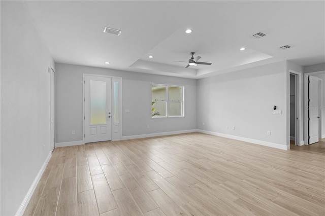 empty room with light hardwood / wood-style floors, a raised ceiling, and ceiling fan