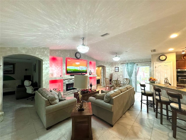 living room featuring a textured ceiling, vaulted ceiling, a fireplace, and light tile flooring