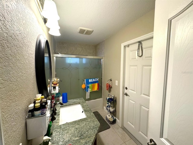 bathroom with tile floors, bath / shower combo with glass door, vanity, and a textured ceiling