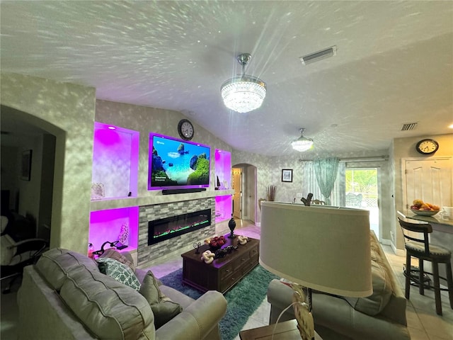 living room with a textured ceiling, tile floors, a stone fireplace, a notable chandelier, and vaulted ceiling