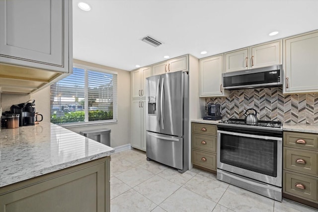 kitchen with appliances with stainless steel finishes, backsplash, light tile floors, and light stone counters