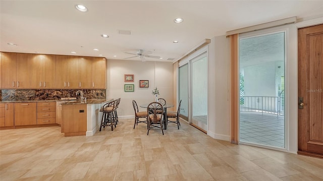 kitchen featuring ceiling fan, tasteful backsplash, dark stone countertops, kitchen peninsula, and a breakfast bar area