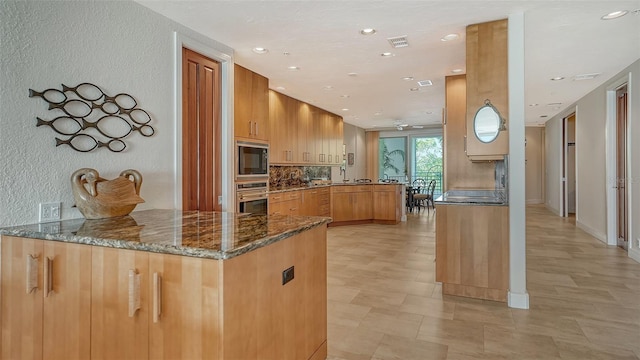 kitchen featuring dark stone counters, oven, decorative backsplash, kitchen peninsula, and black microwave