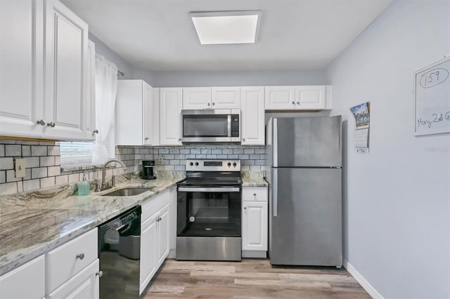 kitchen featuring light stone countertops, light wood-type flooring, white cabinets, appliances with stainless steel finishes, and sink