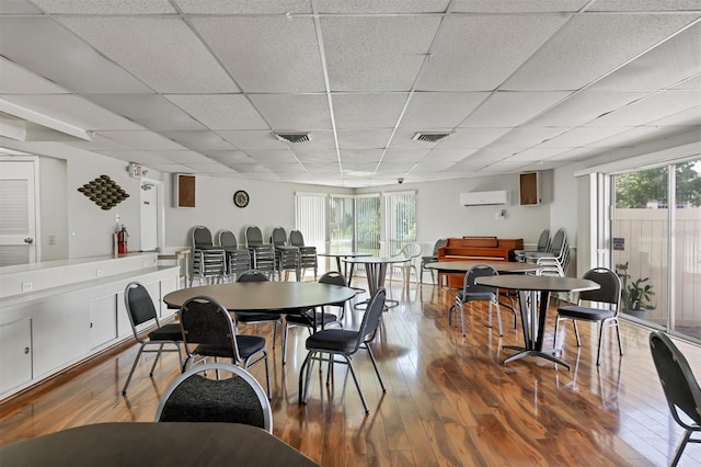 dining area featuring a paneled ceiling, a wealth of natural light, a wall unit AC, and wood-type flooring