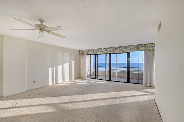 carpeted spare room with ceiling fan, a beach view, a water view, and a healthy amount of sunlight