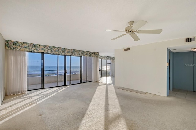 unfurnished room with ceiling fan, light carpet, and a water view