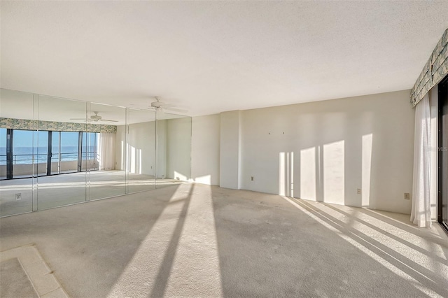 carpeted empty room featuring a textured ceiling, ceiling fan, and a water view