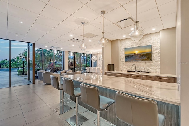 kitchen featuring sink, a kitchen bar, hanging light fixtures, and light stone countertops