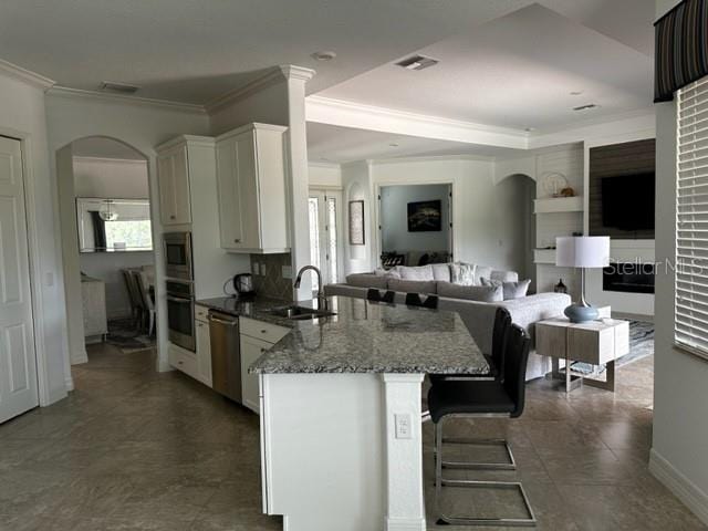 kitchen featuring sink, stainless steel appliances, dark stone counters, a breakfast bar, and white cabinets