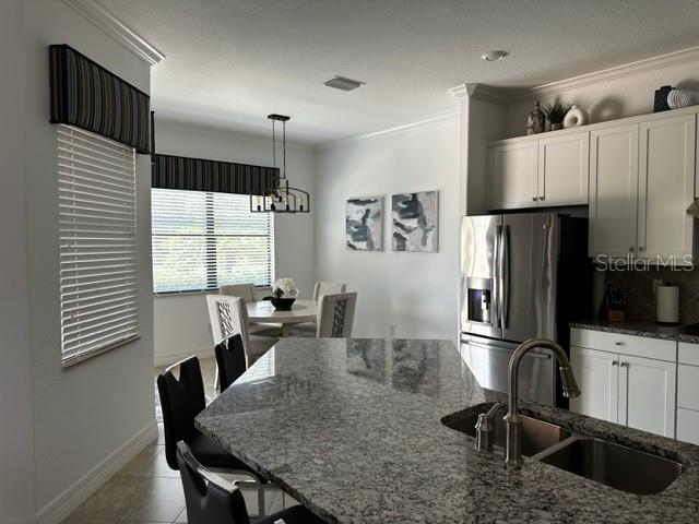 kitchen featuring pendant lighting, sink, stainless steel refrigerator with ice dispenser, dark stone countertops, and white cabinetry