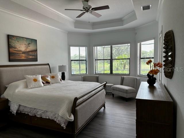 bedroom with dark hardwood / wood-style flooring, a tray ceiling, ceiling fan, and ornamental molding