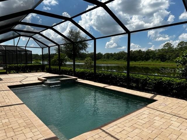 view of pool with glass enclosure, an in ground hot tub, a patio area, and a water view