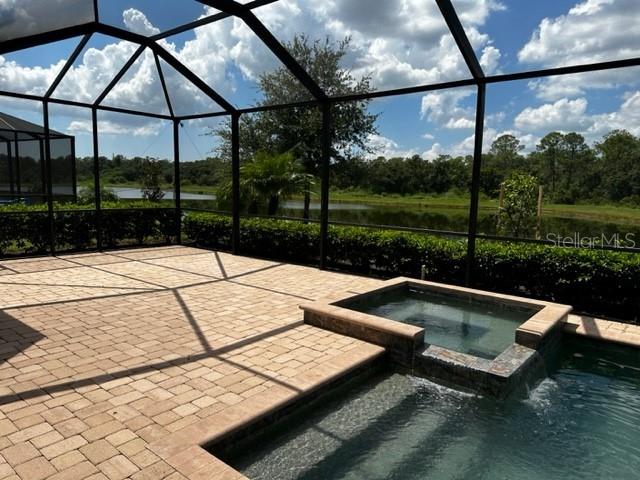 view of patio featuring a swimming pool with hot tub, a water view, and glass enclosure