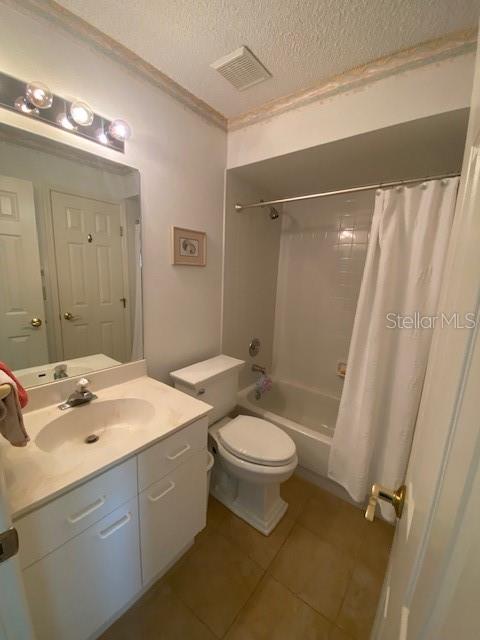 full bathroom featuring toilet, tile flooring, shower / tub combo, vanity, and a textured ceiling