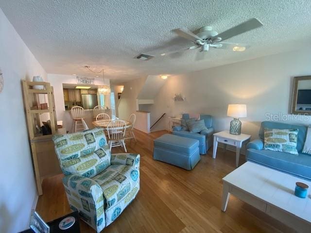 living area with a ceiling fan, a textured ceiling, visible vents, and wood finished floors