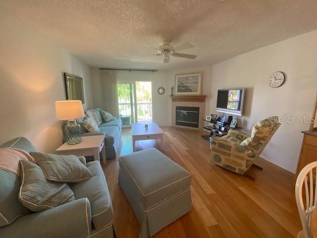 living area with ceiling fan, a textured ceiling, wood finished floors, and a glass covered fireplace