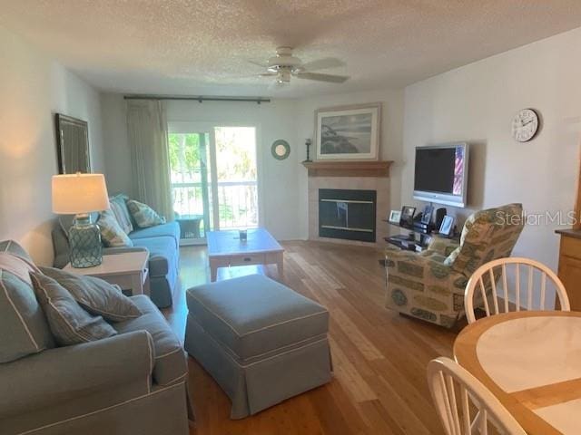 living area with ceiling fan, a textured ceiling, wood finished floors, and a glass covered fireplace