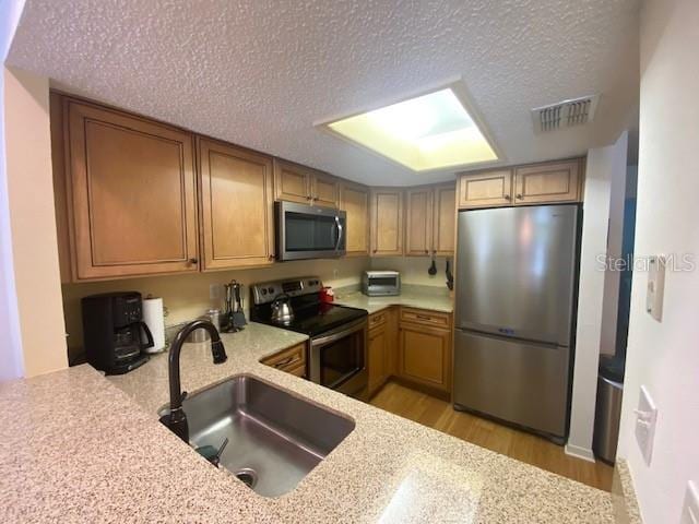 kitchen featuring a textured ceiling, stainless steel appliances, a sink, visible vents, and light wood finished floors