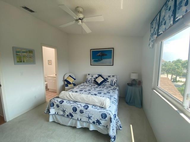 carpeted bedroom with lofted ceiling, visible vents, ceiling fan, and ensuite bath