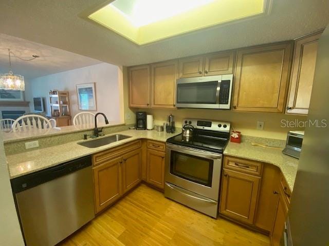 kitchen with a peninsula, stainless steel appliances, light countertops, light wood-style floors, and a sink