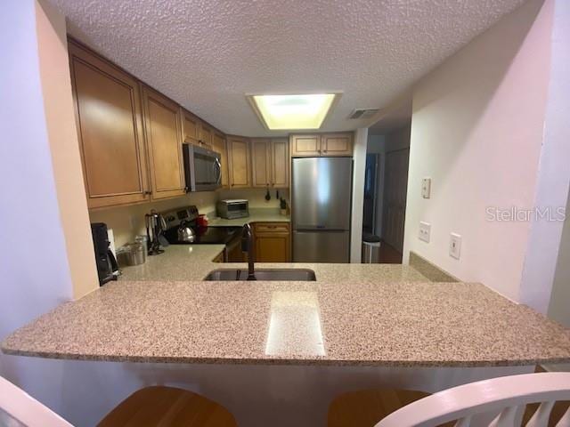 kitchen featuring appliances with stainless steel finishes, a kitchen breakfast bar, a peninsula, a textured ceiling, and a sink