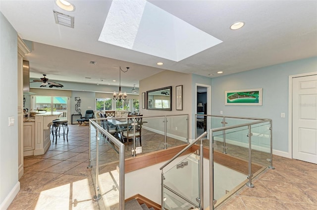 kitchen featuring hanging light fixtures, a skylight, light tile floors, and ceiling fan with notable chandelier