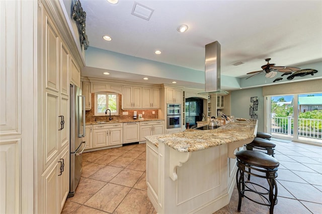 kitchen with ceiling fan, backsplash, light tile floors, sink, and a breakfast bar area