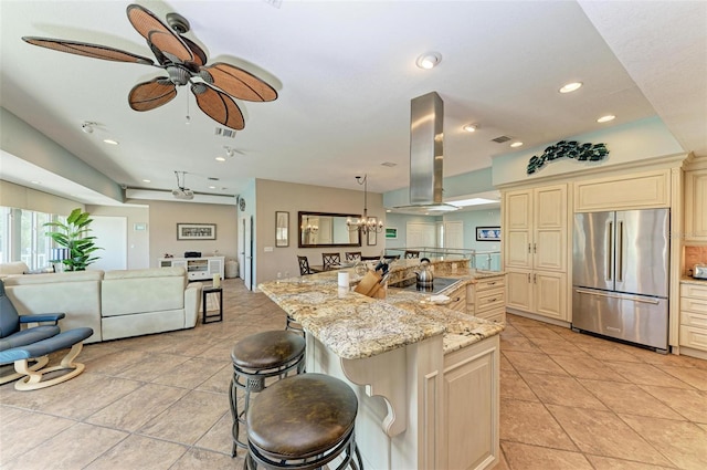 kitchen featuring high end fridge, cream cabinets, island range hood, a kitchen bar, and an island with sink