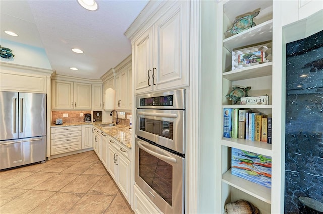 kitchen with light stone counters, light tile flooring, backsplash, appliances with stainless steel finishes, and sink