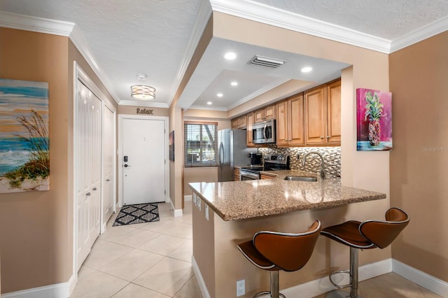 kitchen featuring tasteful backsplash, light stone counters, ornamental molding, a kitchen bar, and appliances with stainless steel finishes