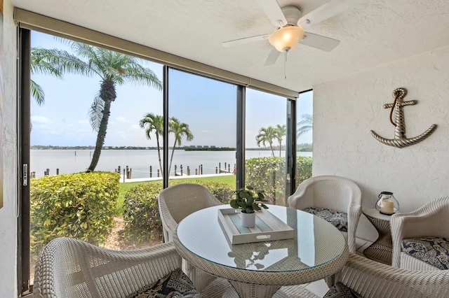 sunroom with ceiling fan and a water view