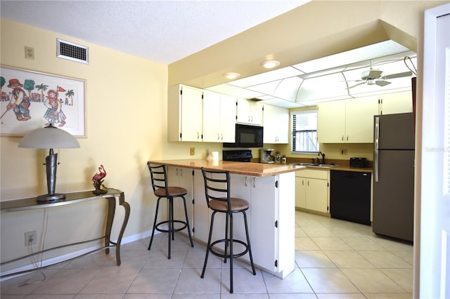 kitchen featuring kitchen peninsula, black appliances, white cabinets, sink, and a breakfast bar