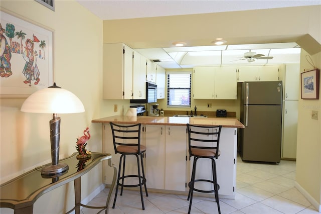 kitchen with ceiling fan, kitchen peninsula, white cabinets, a kitchen bar, and stainless steel refrigerator