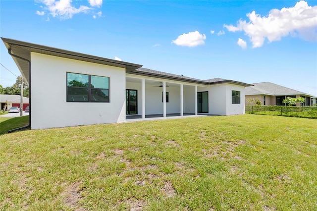 rear view of property featuring a patio area, stucco siding, a ceiling fan, and a yard